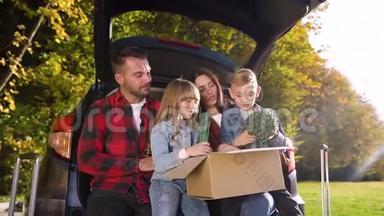 他们的<strong>好孩子</strong>坐在汽车`的后备箱里，手里拿着一个绿花的大盒子，这让父母感到满意